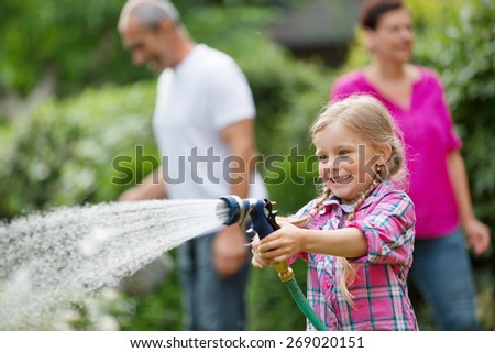 Girl watering plants in garden, family in background