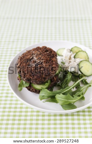Black-bean-burger with rocket, curd and cucumber on plate, vegetarian