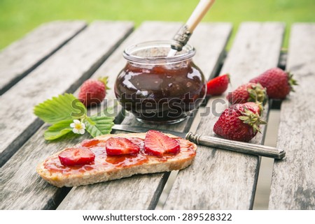Strawberry jam, strawberries, bread with jam on garden table