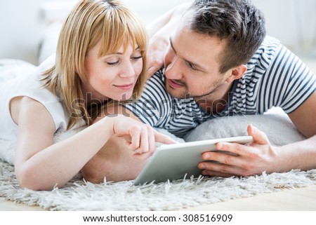 Couple with tablet lying on floor and surfing the net