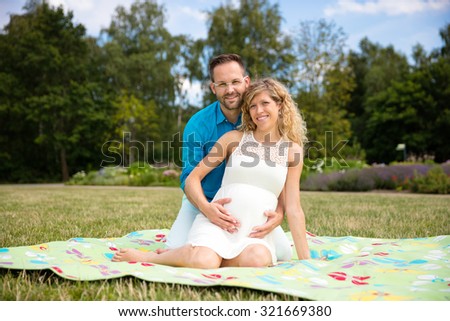 Happy couple expecting baby, sitting on blanket in park