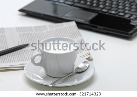 Close up of coffee cup with newspaper and laptop in background