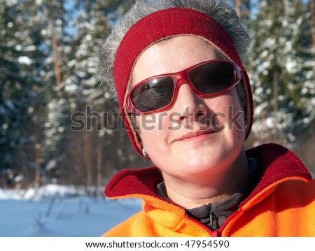 Portrait of senior woman  in front of snow-covered trees with the reflection of the winter landscape in glasses