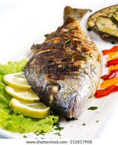 Grilled gilt head sea bream on plate with lemon salad and grilled vegetables