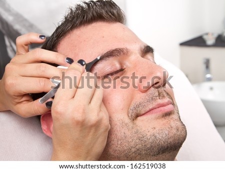 Beautician plucking a beautiful man eyebrows with tweezers in a beauty salon