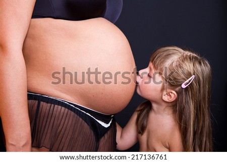 Child kissing belly of pregnant woman against black background