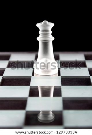 Glass chess queen on chess board over black