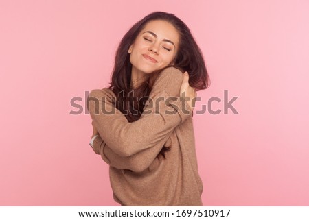 I am egoist, love myself! Portrait of selfish narcissistic young woman with brunette hair embracing herself and smiling with dreamy satisfied expression. indoor studio shot isolated on pink background 商業照片 © 