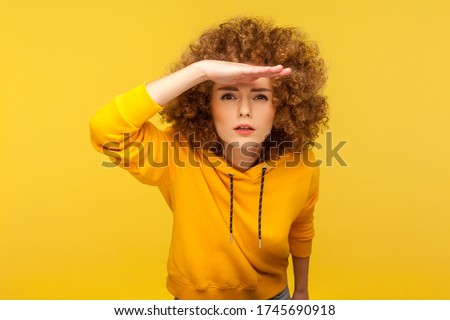 Portrait of curious curly-haired woman in urban style hoodie holding hand above eyes and peering into distance, looking far away, expecting and searching someone on horizon. studio shot isolated Stock foto © 
