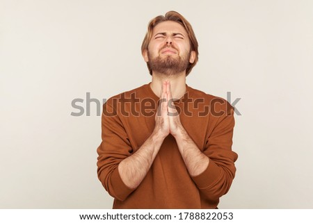 Sincere request to god. Portrait of imploring man with beard in sweatshirt praying up heartily, feeling guilty, pleading begging help from heaven. indoor studio shot isolated on gray background Imagine de stoc © 