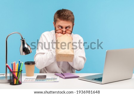 Funny nervous man office worker feeling sick rolling eyes, breathing into paper bag to improve well-being, overcoming stress at work. Indoor studio shot isolated on blue background Photo stock © 