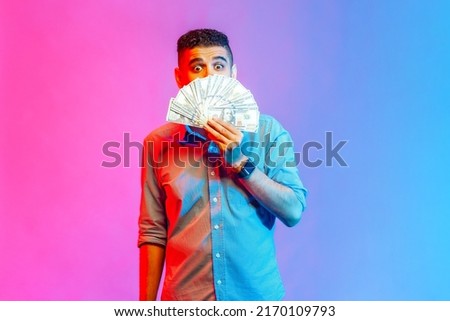 Portrait of young adult attractive man in shirt standing, keeking and demonstrating fan of money and looking at camera. Indoor studio shot isolated on colorful neon light background. Stock fotó © 