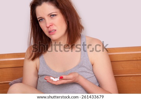 Desperate and sick. young sick woman with red nose sitting on bed and holding pills