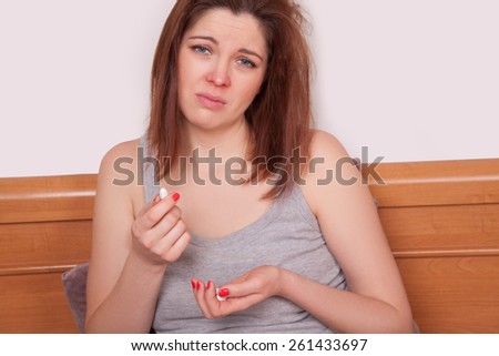 Desperate and sick. young sick woman with red nose sitting on bed and holding pills