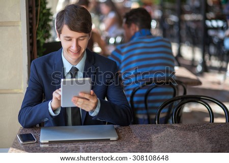 One relaxed young handsome professional businessman working with his laptop, phone and tablet in a noisy cafe. holding and working with tablet.