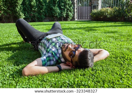 One fashion middle eastern man with beard, fashion hair style is resting on beautiful green grass day time. young arab businessman 20-30 years, resting after hard work. smart phone, tablet. looking