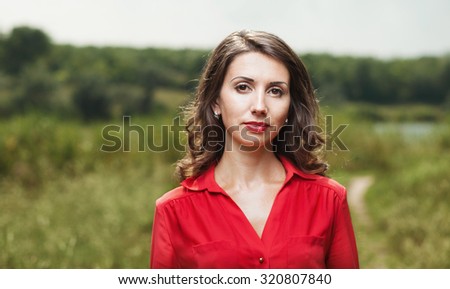 beautiful young girl in red blouse on a background of green nature in summer