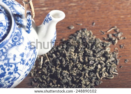 Old Chinese porcelain teapot, with green tea on the wooden desk with soft blue filter