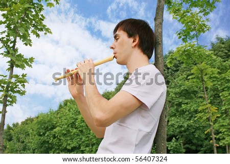 young man playing on flute at summer time outdoor side view