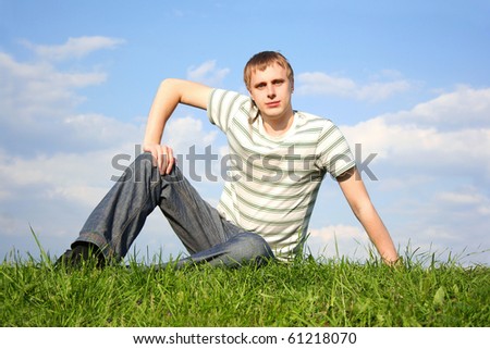 young handsome man lying on summer lawn, hand on knee, looking at camera