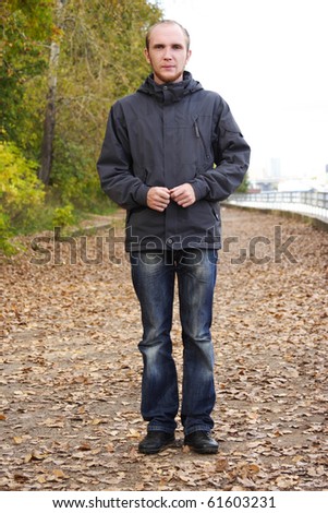 young man with beard standing on path in autumn park, full body