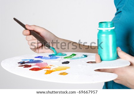 closeup of woman in blue shirt mixing paint on palette