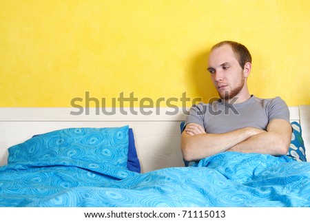 young sad man lying in double bed and looking on empty seat, bright interior