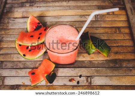 Full glass of a creamy and bubbly watermelon shake smoothie with a slice of watermelon and glass tube. Sliced watermelon and paper decorative on brown wood board  background in rustic style.