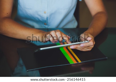 One light-skinned hand belonging to a woman holds a large tablet while the other hand uses a pointer finger to access something on the tablets touch screen display.