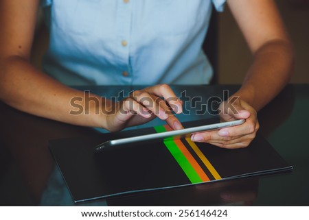 One light-skinned hand belonging to a woman holds a large tablet while the other hand uses a pointer finger to access something on the tablets touch screen display.  The woman in blue shirt.