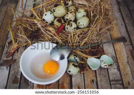 quail spotted eggs in a twig nest spoon, broken egg on a plate on brown background board