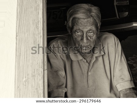 A black and white capture of an old Asian man sitting alone in a doorway. This is an editorial photo taken July 3rd, 2015 in Bangkok Thailand.