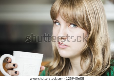 Portrait of a young woman making an ugly face and holding a cup of coffee.