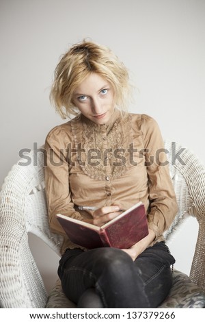Portrait of a blonde woman with blue eyes sitting in her wicker chair writing in a journal.