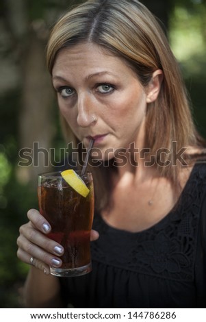 Portrait of a blonde woman with blue eyes outdoors and glass of iced tea with lemon.