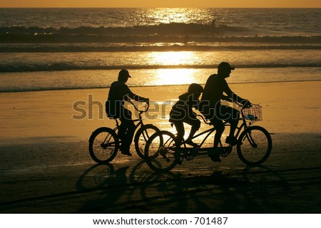 Parents and a child riding bikes along the beach at sunset
