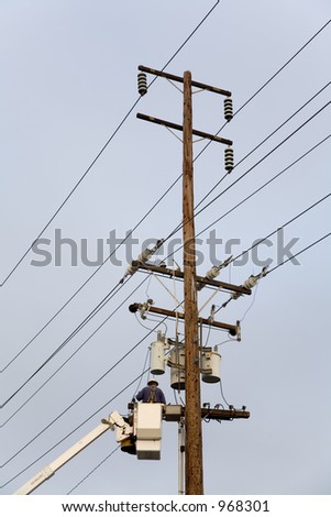 Power company worker wearing a hardhat is repairing electrical wires from a utility bucket truck.
