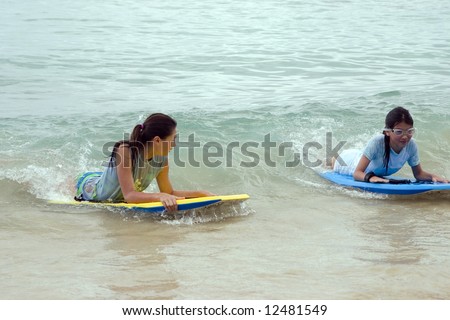 sisters playing in the ocean on boogie boards