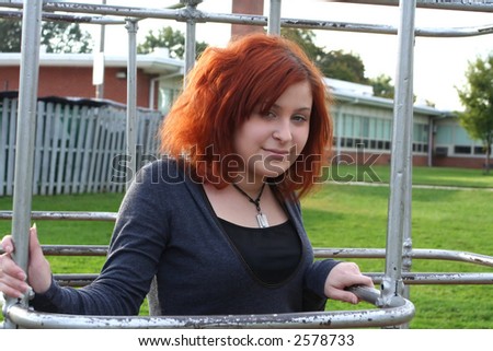 Contemporary teen girl inside playground monkey bars on school grounds.