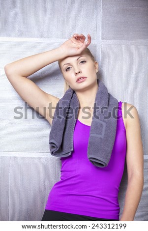 Pretty blonde woman after fitness training standing tired against the wall