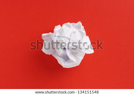 A scrunched up ball of white printing or writing paper in the center of a red paper background