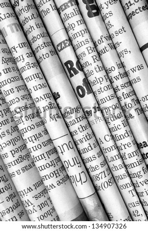 A black and white background of English language newspapers folded and stacked in a diagonal position and viewed in close up