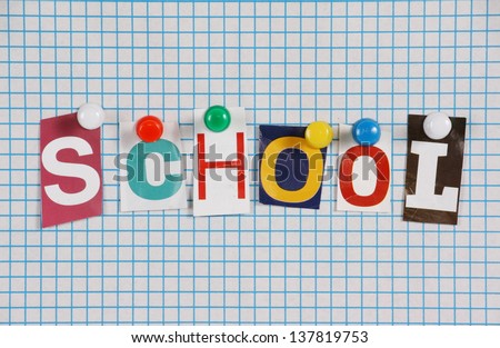 The word School in cut out magazine letters pinned to blue lined graph paper background