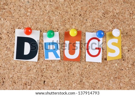 The word Drugs in cut out magazine letters pinned to a cork notice board