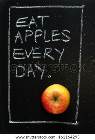 Eat Apples Every Day written by hand on a blackboard sign, next to a single yellow and red apple of the Zari variety