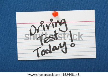A reminder of a Driving Test Today written on a white note card pinned to a blue notice board.