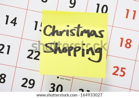 Christmas Shopping reminder written on a yellow paper adhesive note stuck to a wall calendar background