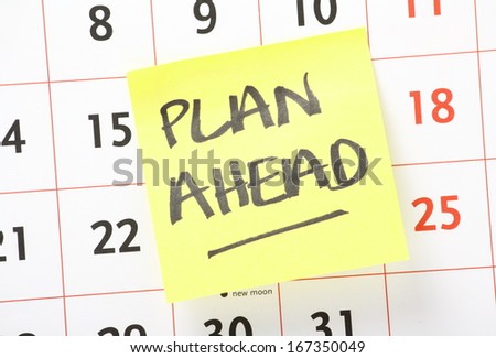 The phrase Plan Ahead written on a yellow sticky paper note and stuck on a wall calendar background