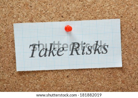The phrase Take Risks typed on a piece of graph paper and pinned to a cork notice board