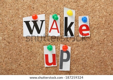 The phrase Wake Up in cut out magazine letters pinned to a cork notice board